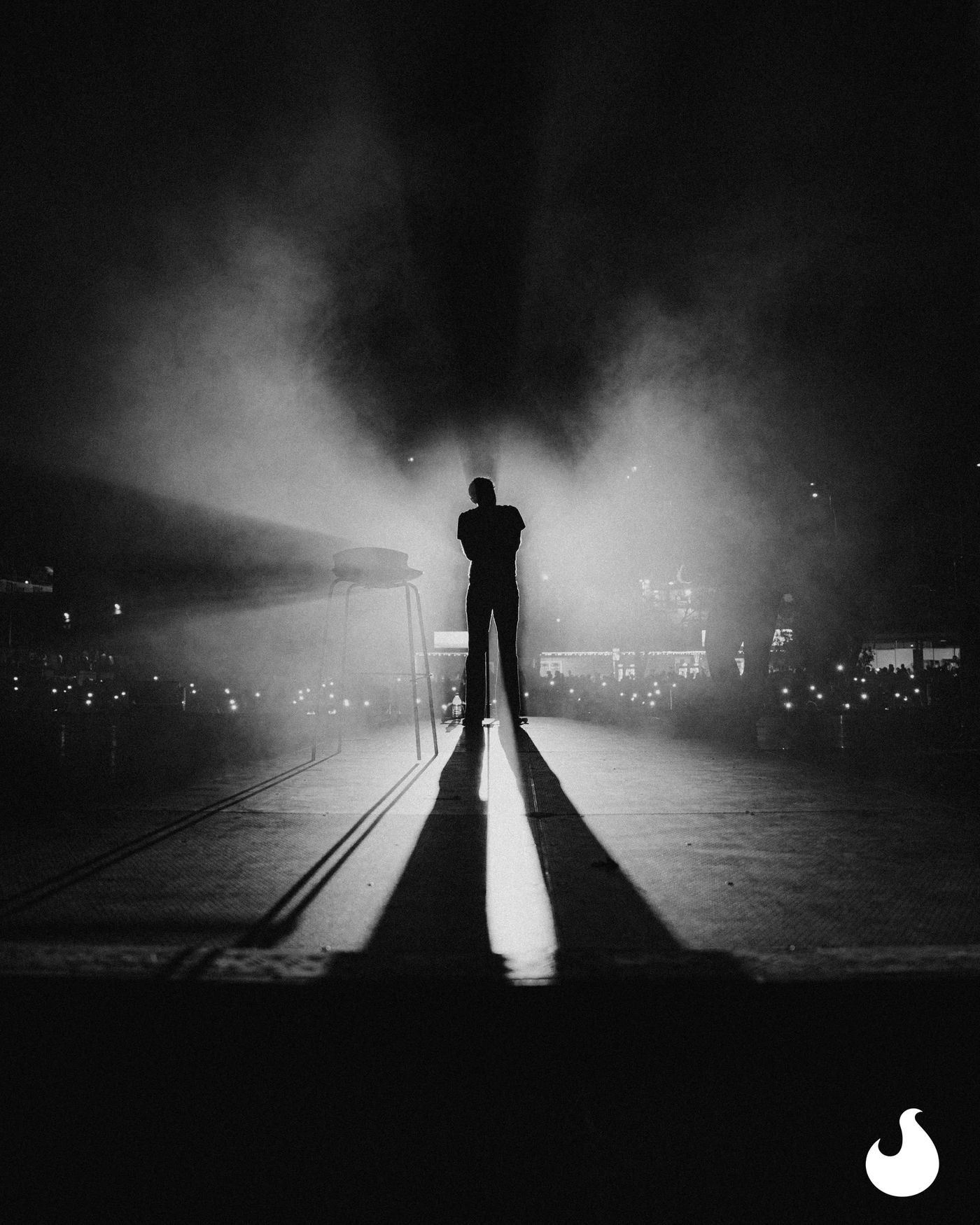 Un artista in controluce sul palco, in bianco e nero, dentro il fumo.